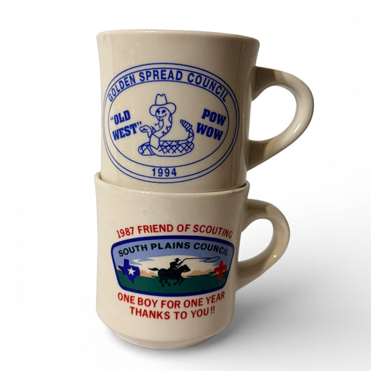Two ceramic mugs with vintage scout-themed designs stacked on a white background