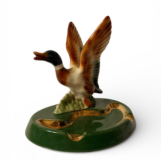 Ceramic duck figurine on a green base with a white background